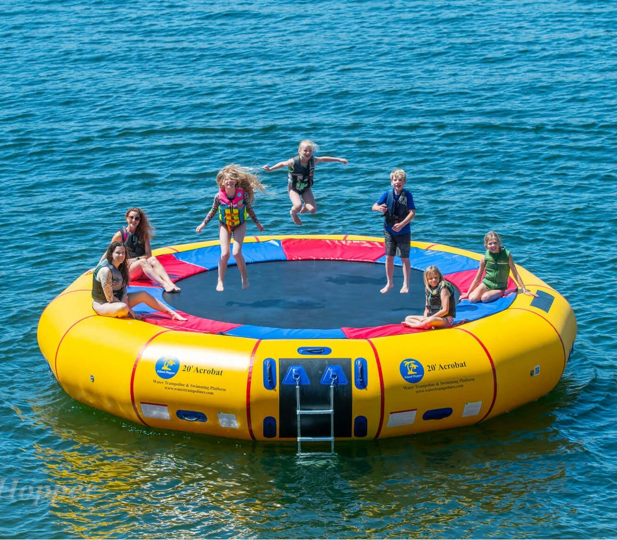 Family jumping on Island Hopper 20ft Acrobat steel frame water trampoline on the lake in summer