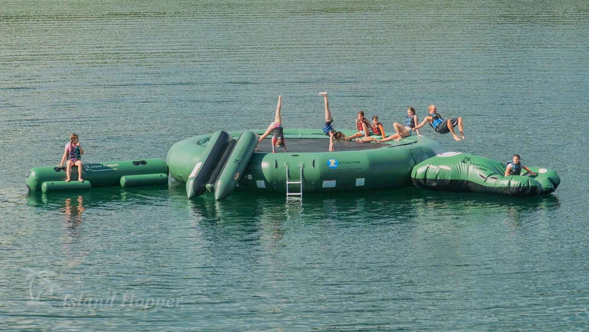 Group on Island Hopper 25ft Giant Jump natural green steel frame water trampoline on the lake in summer